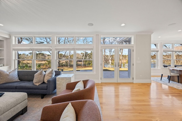 living room featuring crown molding, built in features, french doors, and light wood-type flooring