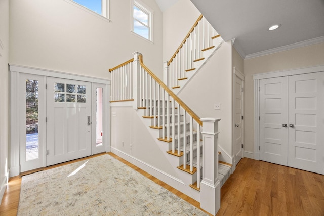 foyer with a towering ceiling, ornamental molding, and light wood-type flooring