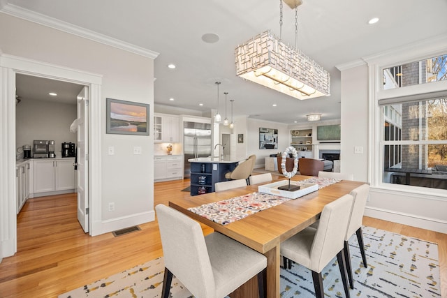 dining room featuring crown molding, sink, built in features, and light hardwood / wood-style floors