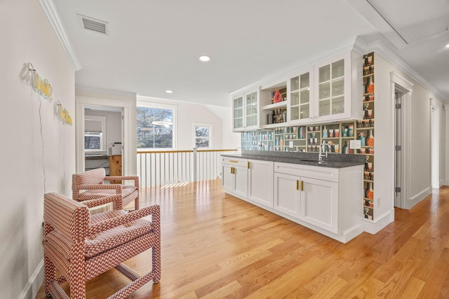 bar with light wood-type flooring, crown molding, sink, and white cabinets