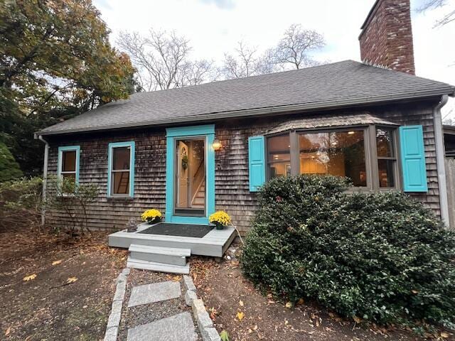 view of front facade featuring roof with shingles and a chimney