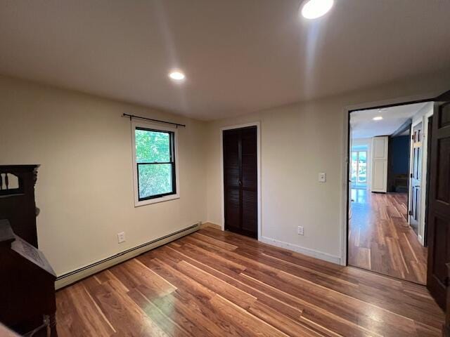 unfurnished bedroom featuring baseboards, a baseboard heating unit, wood finished floors, and recessed lighting