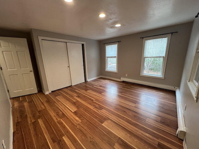 unfurnished bedroom featuring recessed lighting, a closet, baseboard heating, dark wood-type flooring, and baseboards