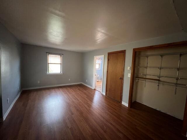 unfurnished bedroom featuring dark wood-type flooring, ensuite bath, baseboards, and two closets