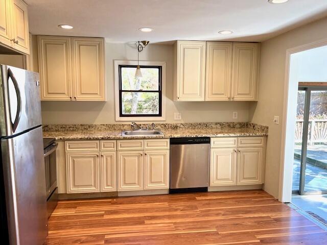 kitchen with decorative light fixtures, appliances with stainless steel finishes, a sink, light stone countertops, and light wood-type flooring