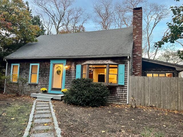 view of front of house with a shingled roof, a chimney, and fence