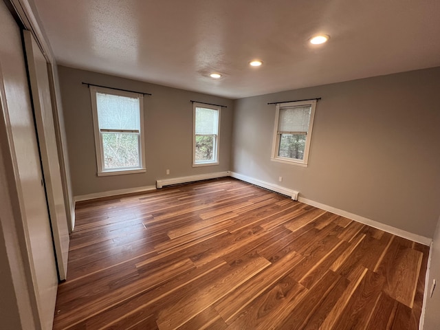 spare room with a baseboard heating unit, baseboards, dark wood-type flooring, and recessed lighting