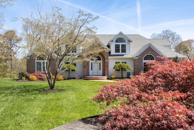 view of front facade featuring a front lawn, brick siding, and a shingled roof