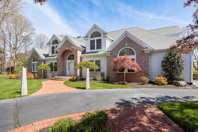 view of front facade featuring a shingled roof, a front lawn, and brick siding