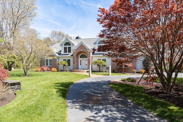 view of front of house featuring a front yard, a chimney, curved driveway, and brick siding