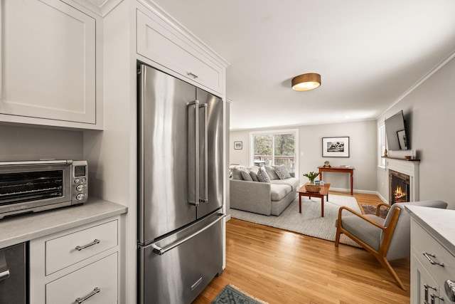 kitchen with light hardwood / wood-style flooring, high quality fridge, crown molding, and white cabinets