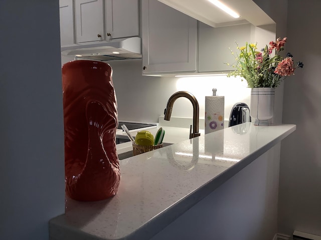 kitchen featuring under cabinet range hood, light stone countertops, and a baseboard heating unit