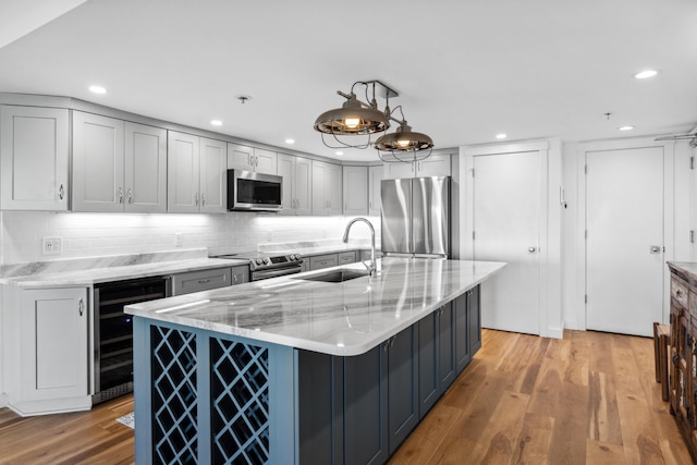 kitchen with decorative light fixtures, sink, beverage cooler, a kitchen island with sink, and stainless steel appliances