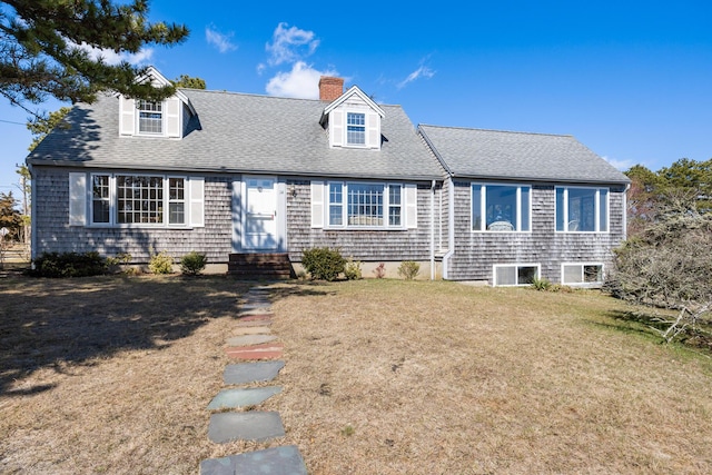 cape cod-style house featuring a front yard, roof with shingles, entry steps, and a chimney