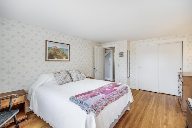 bedroom featuring light wood-type flooring, wallpapered walls, and a closet