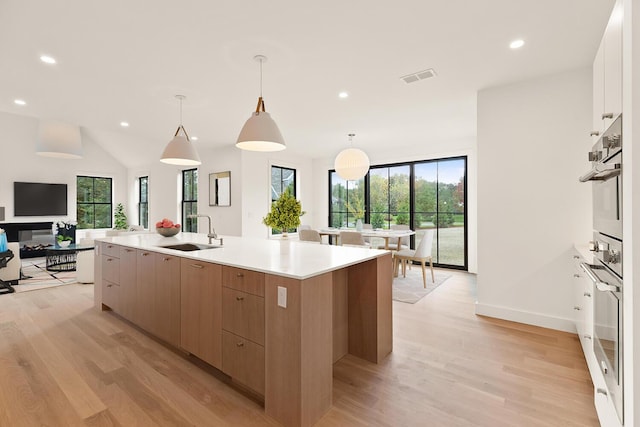 kitchen with sink, light wood-type flooring, pendant lighting, and a spacious island