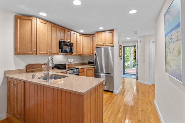 kitchen featuring sink, stainless steel appliances, light stone countertops, kitchen peninsula, and light wood-type flooring