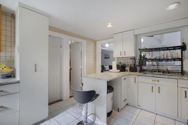 298 Oakland Rd, Hyannis, MA 02601 - kitchen featuring a sink, white cabinetry, light stone countertops, decorative backsplash, and light tile patterned flooring