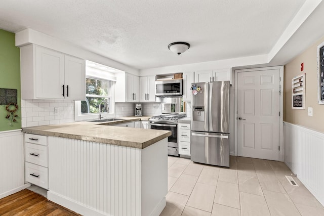 kitchen with tasteful backsplash, sink, white cabinets, stainless steel appliances, and light tile patterned flooring