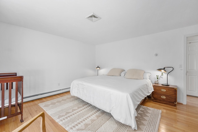 bedroom with visible vents, baseboard heating, and light wood-type flooring