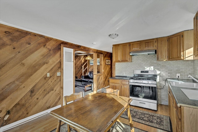 kitchen featuring extractor fan, wooden walls, sink, stainless steel range with gas stovetop, and light hardwood / wood-style flooring