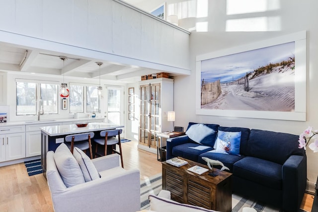 living room with french doors, beam ceiling, sink, and light wood-type flooring