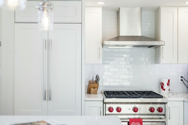 kitchen featuring high end appliances, wall chimney exhaust hood, decorative backsplash, and white cabinets