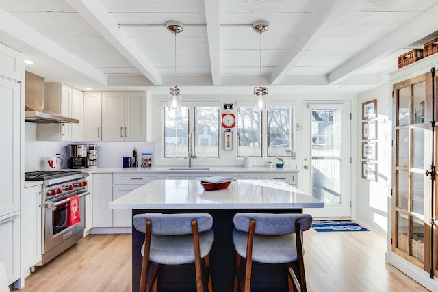 kitchen with wall chimney exhaust hood, light hardwood / wood-style flooring, pendant lighting, high end stove, and white cabinets