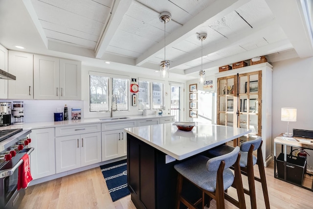 kitchen with beamed ceiling, sink, white cabinets, high end stainless steel range, and light hardwood / wood-style floors