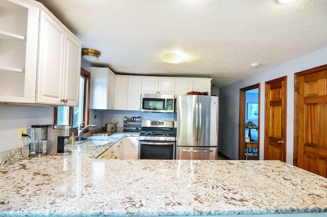 59 Whitecaps Dr, East Falmouth, MA 02536 - kitchen with appliances with stainless steel finishes, light stone counters, white cabinets, a peninsula, and open shelves