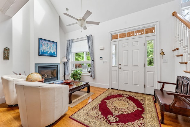 entrance foyer with baseboards, a glass covered fireplace, stairway, vaulted ceiling, and light wood-style floors