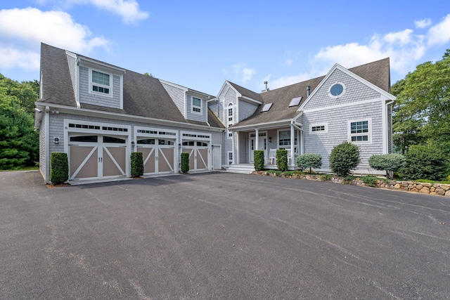 shingle-style home featuring a shingled roof, a porch, and aphalt driveway