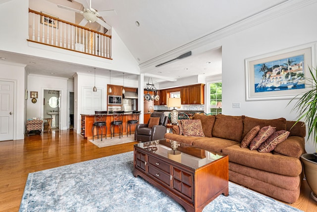 living room with ceiling fan, a high ceiling, ornamental molding, and wood finished floors