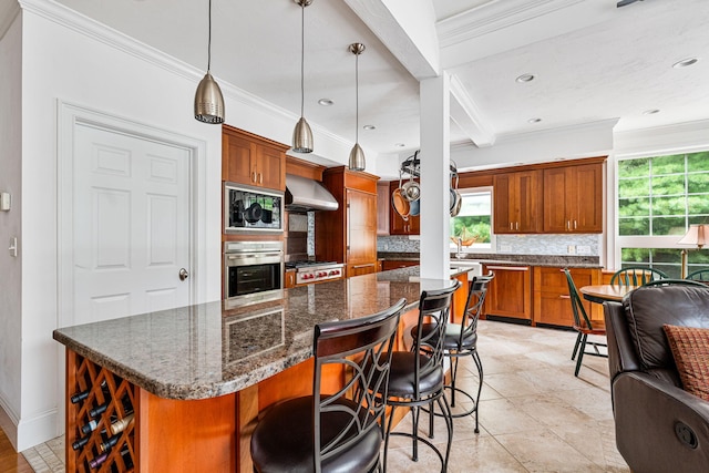 kitchen with brown cabinets, decorative backsplash, stainless steel oven, built in microwave, and wall chimney exhaust hood