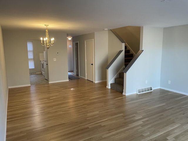 empty room featuring a baseboard radiator, wood-type flooring, and an inviting chandelier