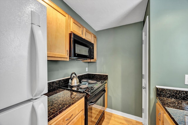 kitchen featuring light brown cabinetry, baseboards, black appliances, dark stone countertops, and light wood-style flooring