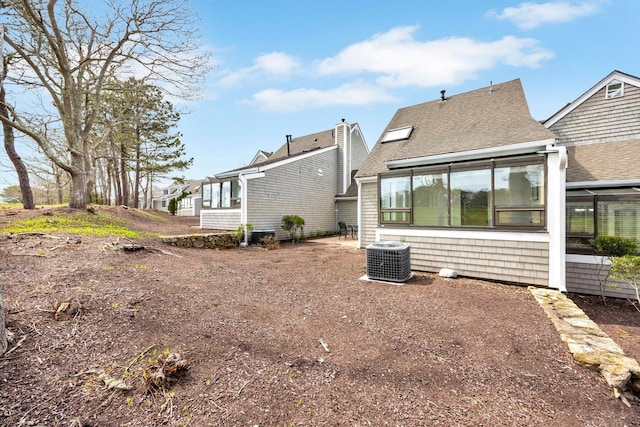 rear view of house with central AC, a shingled roof, and a sunroom
