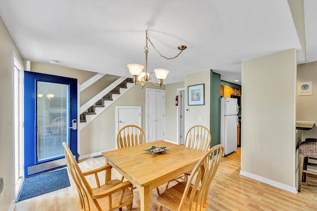 dining space with baseboards, a chandelier, light wood-style flooring, and stairway