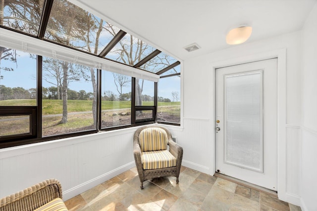 sunroom / solarium with baseboards, stone finish flooring, visible vents, and a wainscoted wall