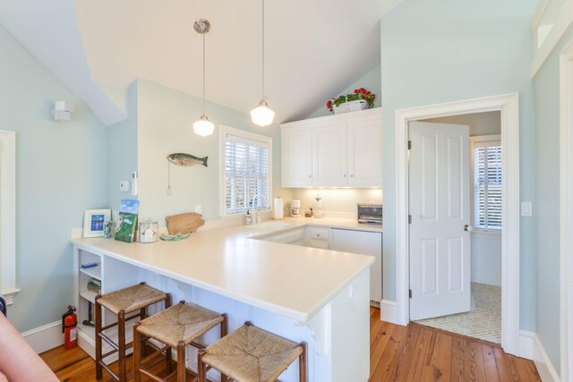 kitchen featuring a sink, a breakfast bar, light wood-type flooring, a peninsula, and white cabinetry