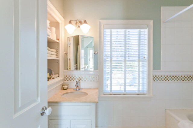 full bath with vanity, a tub to relax in, and tile walls