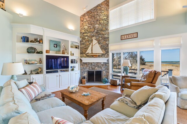 living area featuring a stone fireplace, wood finished floors, and high vaulted ceiling