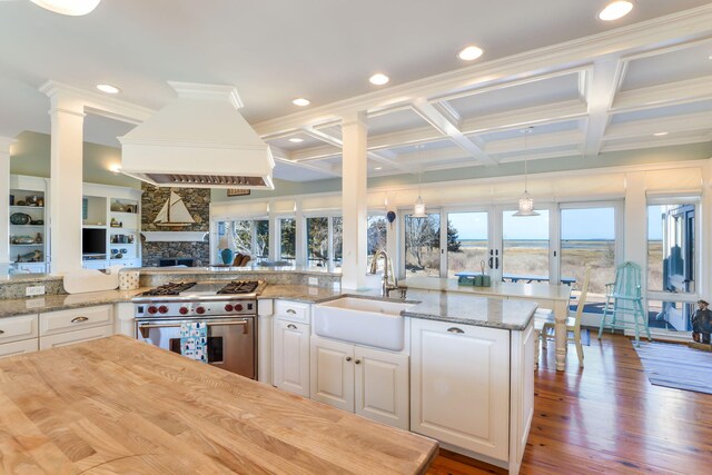 kitchen featuring white cabinets, a sink, high end stove, a stone fireplace, and premium range hood