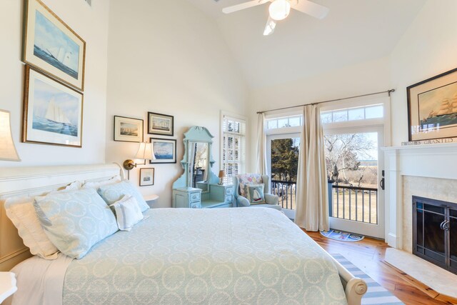 bedroom with high vaulted ceiling, a ceiling fan, wood finished floors, a fireplace with flush hearth, and access to outside