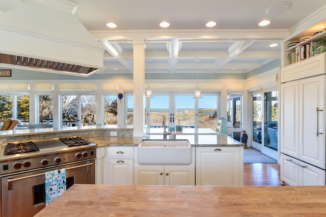 kitchen featuring light stone counters, a sink, high end range, custom range hood, and white cabinetry