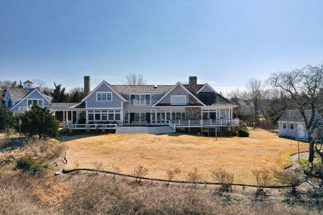 back of house featuring a chimney, an outdoor structure, a deck, and a lawn
