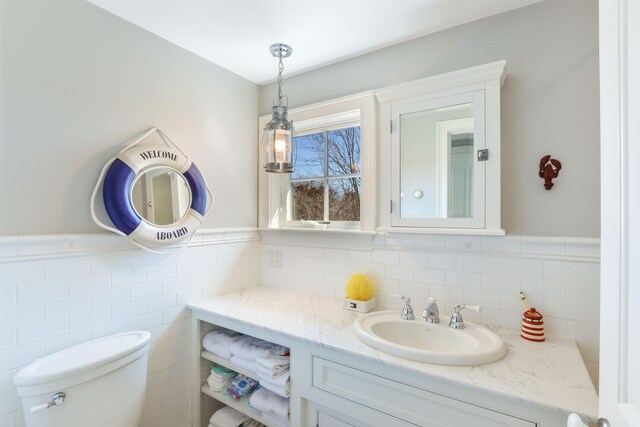 bathroom with wainscoting, toilet, vanity, and tile walls