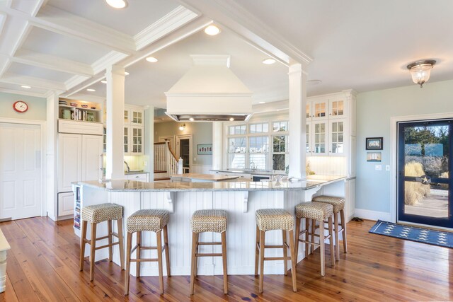 kitchen with a kitchen breakfast bar, decorative columns, wood-type flooring, and premium range hood