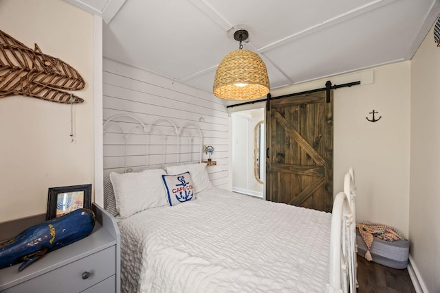 bedroom with wooden walls, baseboards, a barn door, and wood finished floors