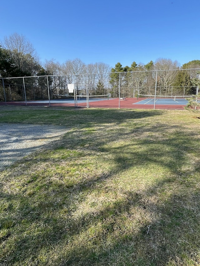 view of tennis court with fence and a lawn